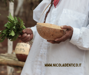 Dettaglio di uno sciamano (curandero) maya. In mano stringe gli elementi utili per eseguire un rito di guarigione: un mazzo d'erbe fresche e una ciotola piena di acqua profumata.